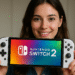 Switch 2 vs Switch 1 - Person holding a white Nintendo Switch 2 handheld with the logo on screen, illustrating a Switch 2 vs Switch 1 design comparison.