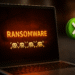 Acceso Controlado a Carpetas: protección contra ransomware en Windows; portátil con aviso "RANSOMWARE" y un icono verde que indica bloqueo de cambios no autorizados.