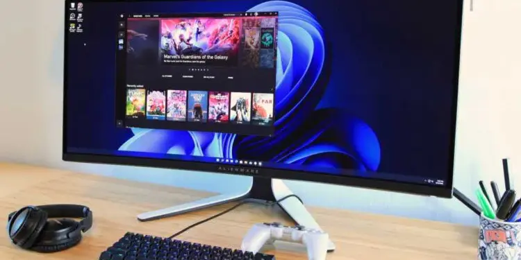 Top monitores gaming: monitor ultrawide curvo Alienware en escritorio, con teclado mecánico, auriculares y mando, ideal para setup de juegos en PC.
