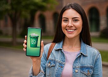 Sampah WhatsApp - Wanita muda tersenyum menunjukkan ikon tempat sampah hijau dengan logo WhatsApp di ponselnya, konsep sampah WhatsApp untuk membersihkan dan mengosongkan ruang ponsel dalam hitungan menit.