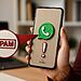 WhatsApp Spam - Teléfono móvil con logo de WhatsApp y advertencia de spam, ilustrando cómo activar el filtro oculto de mensajes no deseados en WhatsApp.