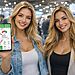 Velocidad de carga real en tu teléfono Android mostrada en una app medidor de carga con amperaje y estado de batería en pantalla, mientras una mujer sostiene el smartphone en una tienda de tecnología.